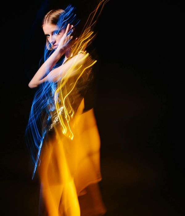 Woman performing a light cardio movement in a dark studio with aurora-colored lights.